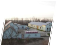 A small tilted photograph shows several low buildings with light-colored roofs among bare trees. Pale ground is visible around the structures. A white angled border frames the photograph.